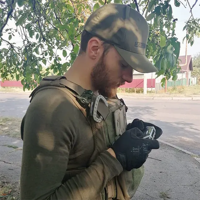 Marcel Neuroth in Einsatzkleidung prüft ein Gerät, im Hintergrund eine Straße in der Ukraine.