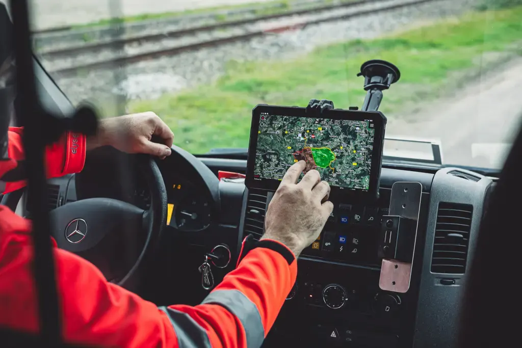 Blick ins Fahrerhaus eines Einsatzfahrzeugs: Eine Einsatzkraft in roter Jacke tippt auf ein Tablet mit ATAK-Karte an der Halterung.