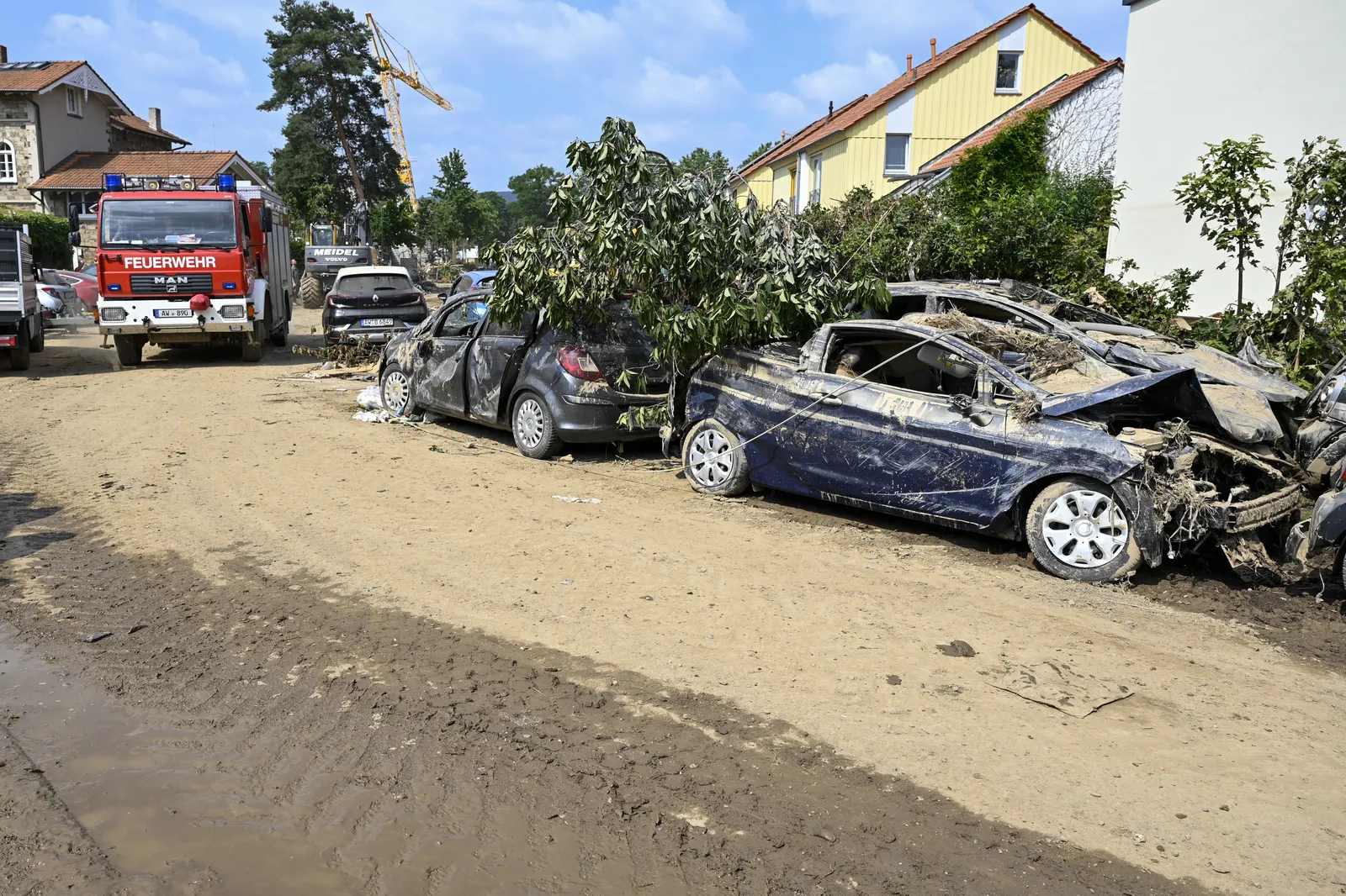 Feuerwehrfahrzeug in einer verschlammten Straße in Ahrweiler, davor von der Flut zerstörte Autos, Juli 2021.