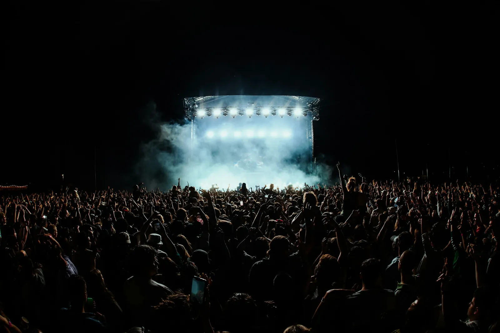 Una gran multitud de noche frente a un escenario al aire libre muy iluminado.