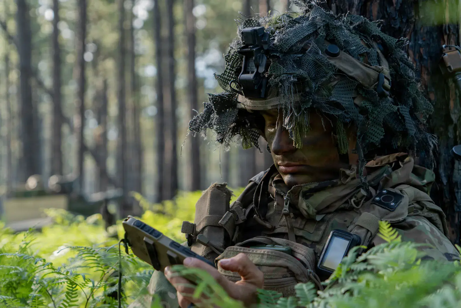Soldado camuflado planifica una ruta con ATAK en un celular resistente en el bosque.