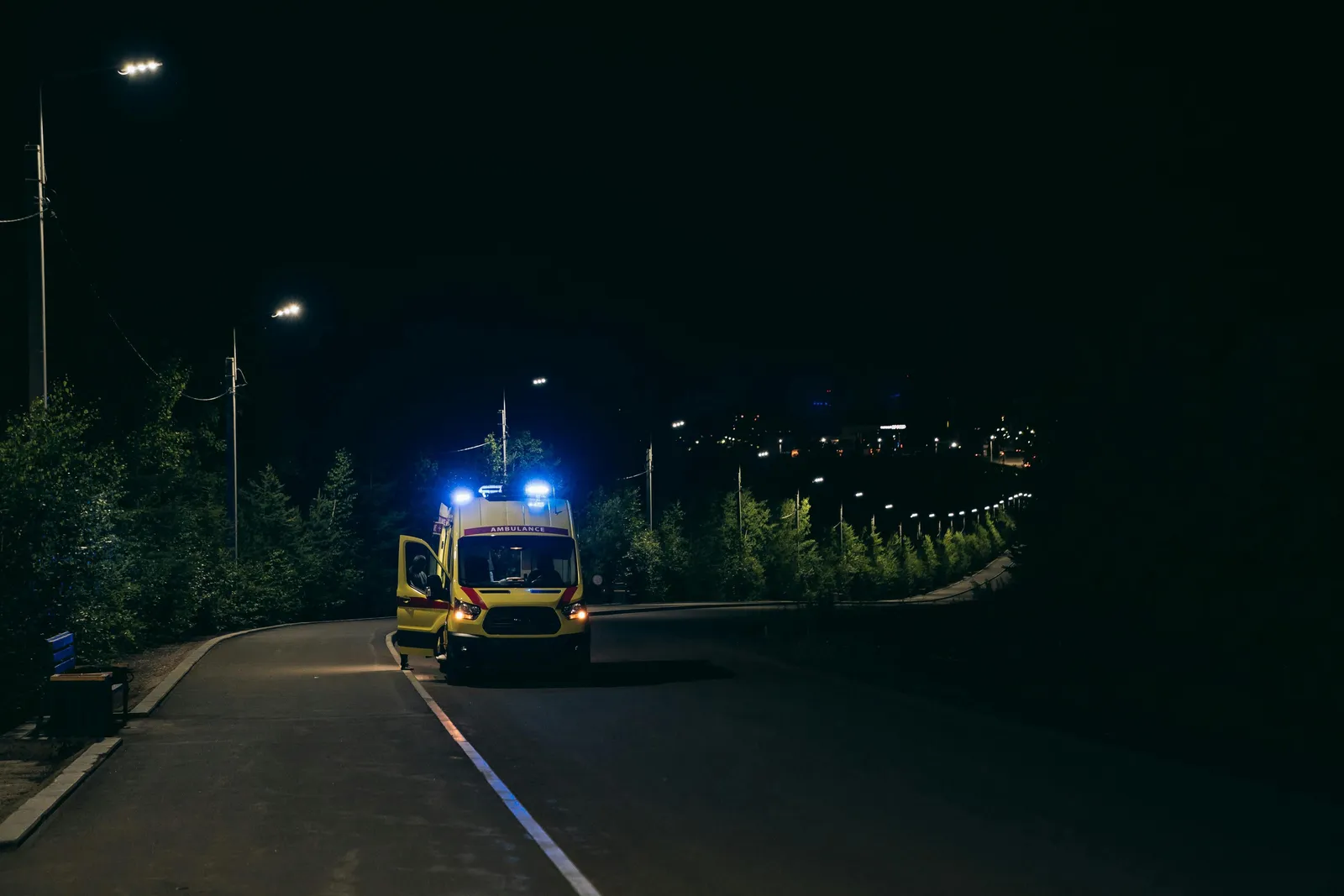 Rettungswagen mit Blaulicht steht nachts mit geöffneter Tür auf einer Straße.