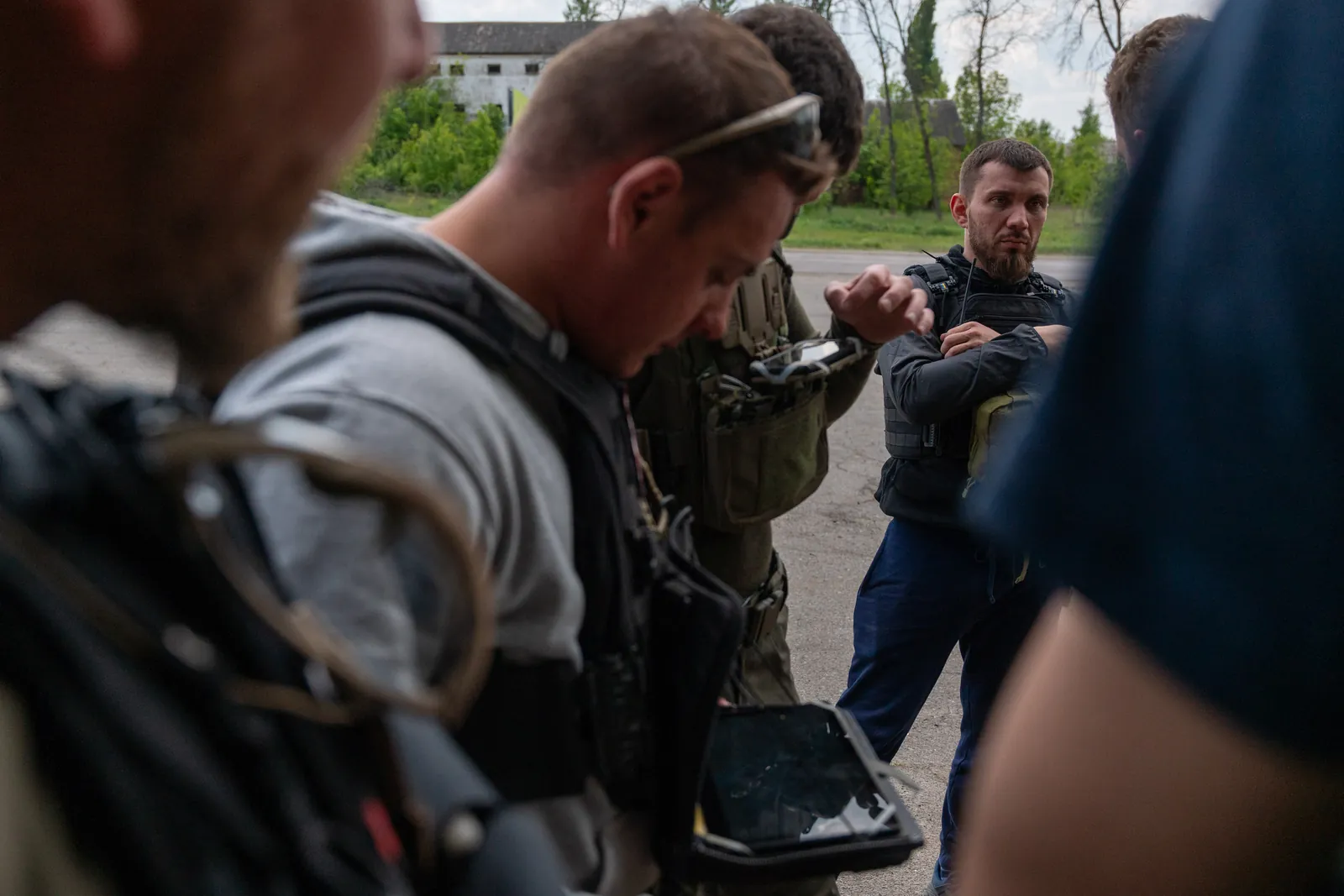 Волонтери в захисних жилетах розмовляють просто неба, один тримає планшет з ATAK.