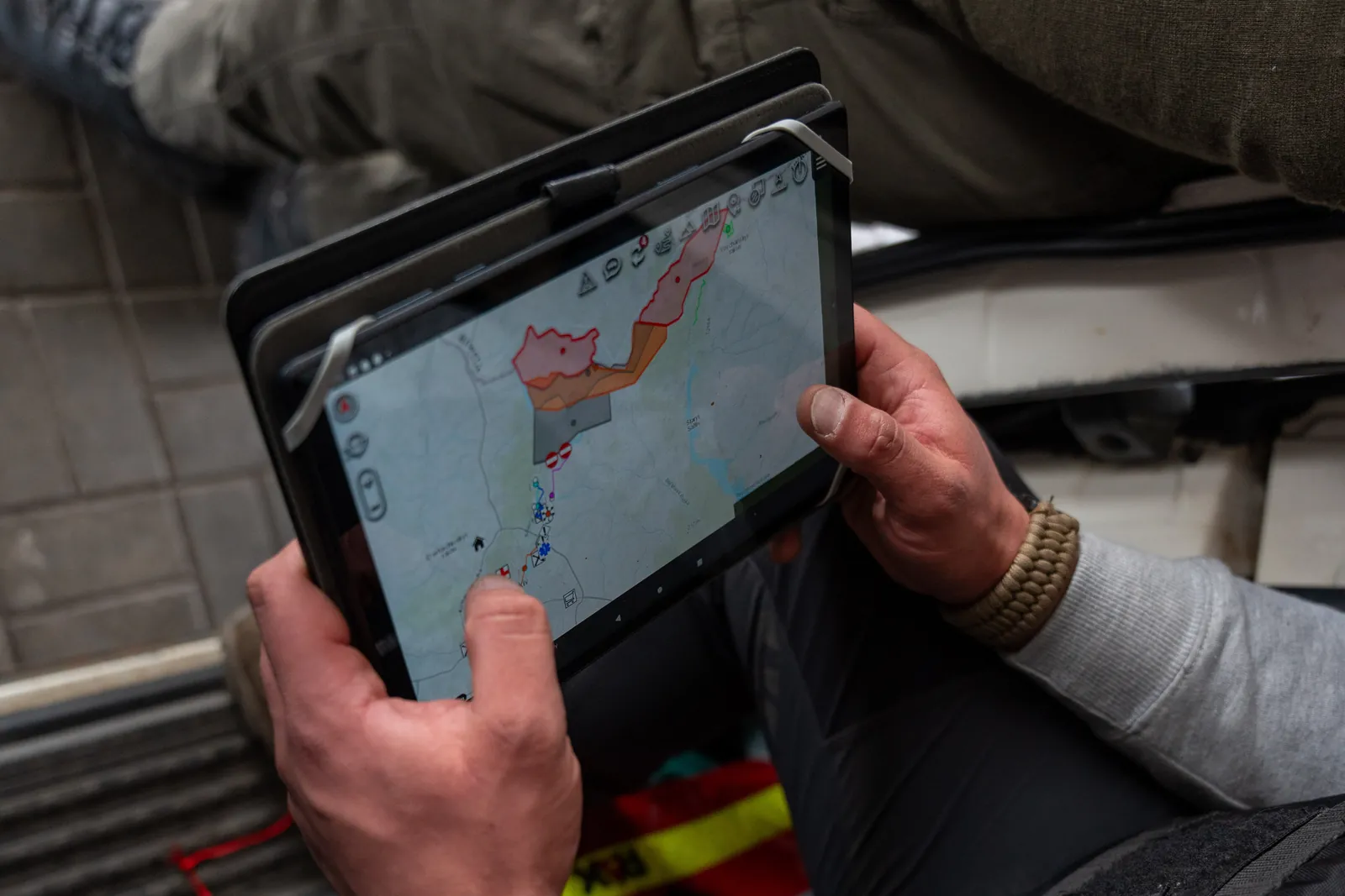 Eine Einsatzkraft sitzt im Fahrzeug und hält ein Tablet mit ATAK, auf der Karte sind Gebiete farbig markiert.